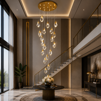 A modern multi-light cluster Astraea Cascade Duplex Chandelier with clear glass droplets and gold-toned metal accents hangs in a grand, contemporary entryway with a staircase and warm ambient lighting.